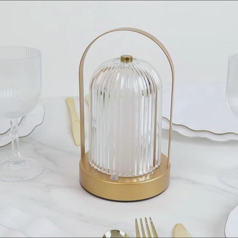 Gold cordless LED table lamp with ribbed acrylic shade on a dining table.