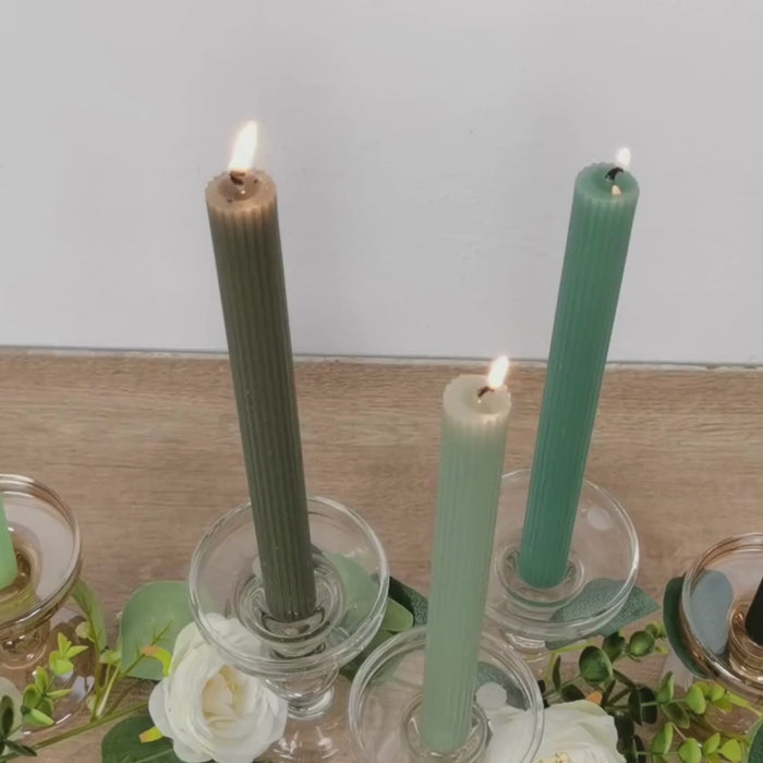 Sage green ribbed taper candles in glass holders with flowers.