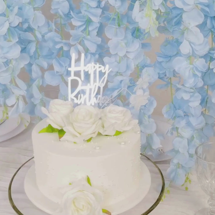 Light blue artificial silk wisteria flower garland hanging behind a white cake.