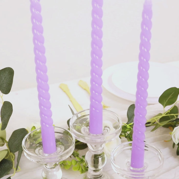 Lavender lilac spiral taper candles in glass holders on a table.