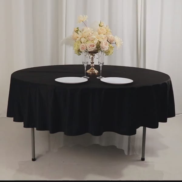 Black round tablecloth on a table with floral centerpiece and plates.