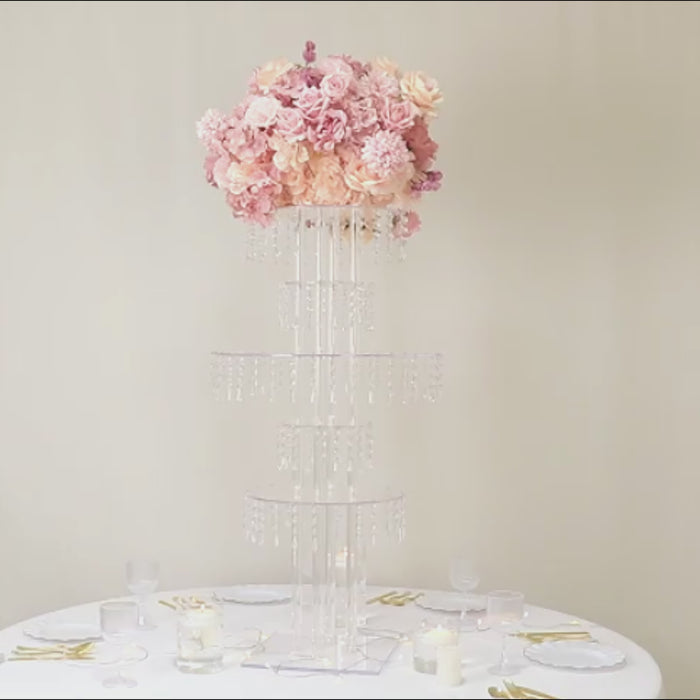 Clear acrylic chandelier flower stand with hanging crystals and pink floral arrangement.
