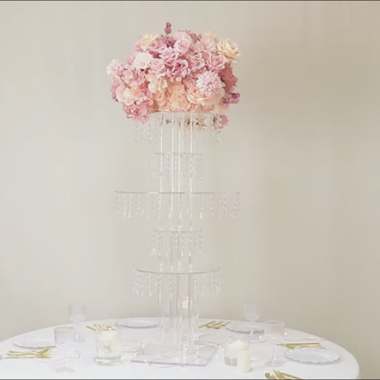 Clear acrylic chandelier flower stand with hanging crystals and pink floral arrangement.