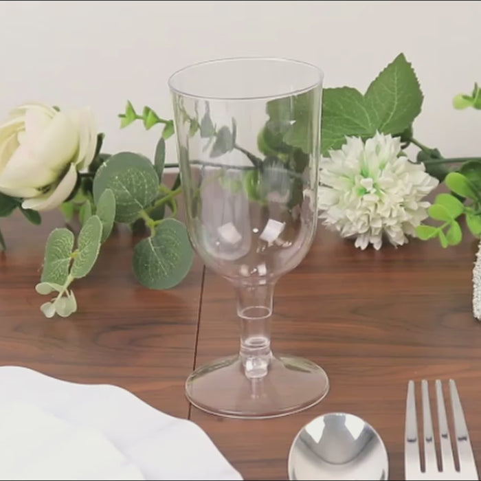 Clear disposable wine glasses with detachable bases on a wooden table.