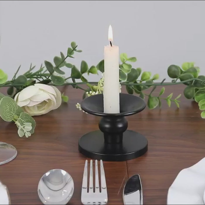 Black metal candle holder with a white candle, elegantly set on a wooden table.