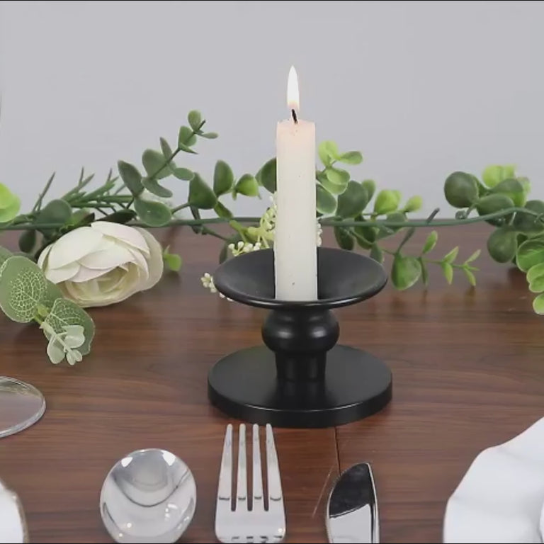 Black metal candle holder with a white candle, elegantly set on a wooden table.