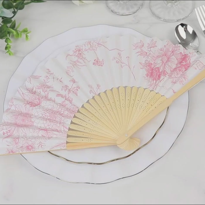 White and pink French toile pattern handheld fan on a table setting.