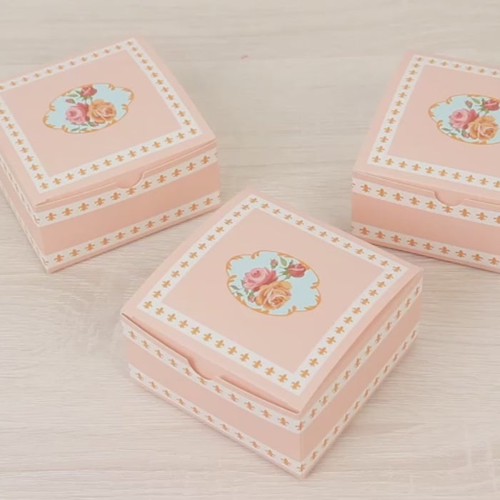 Dusty rose floral favor boxes stacked on a light surface.