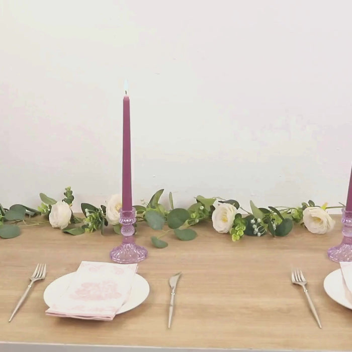 Dusty rose taper candles on a table with floral decor.