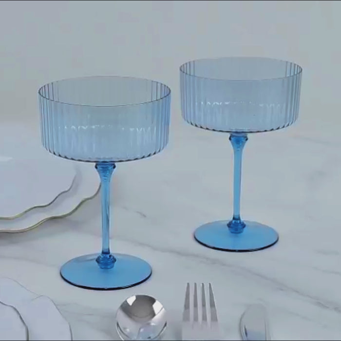 Dusty blue ribbed plastic coupe champagne glasses on a marble surface.