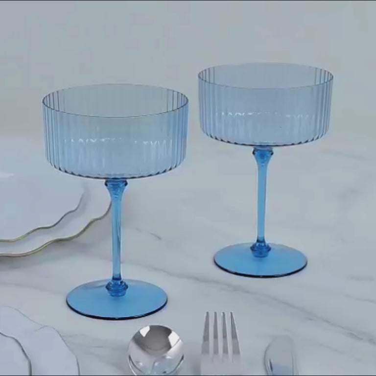 Dusty blue ribbed plastic coupe champagne glasses on a marble surface.