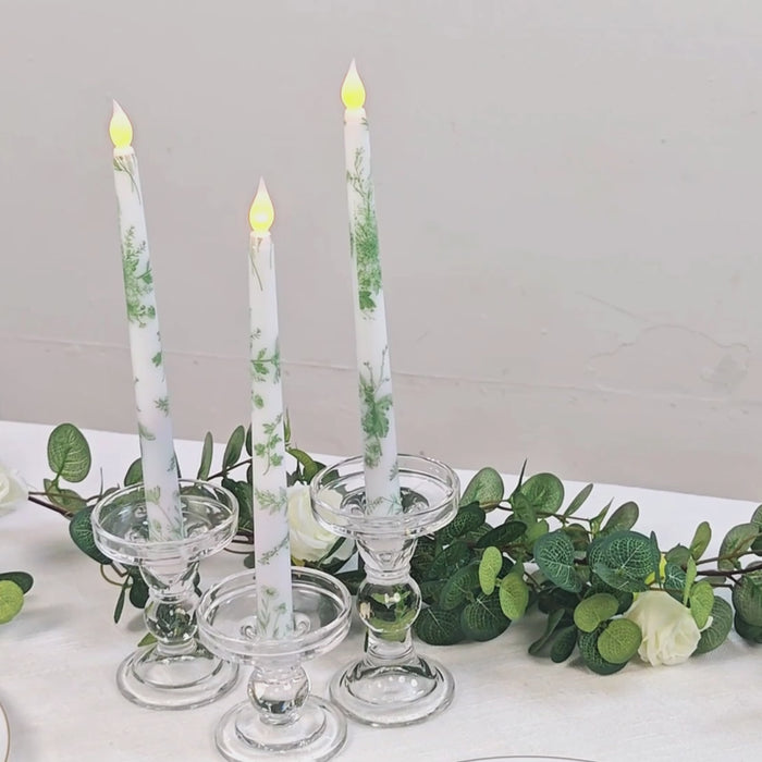 White and sage green flameless taper candles in glass holders.