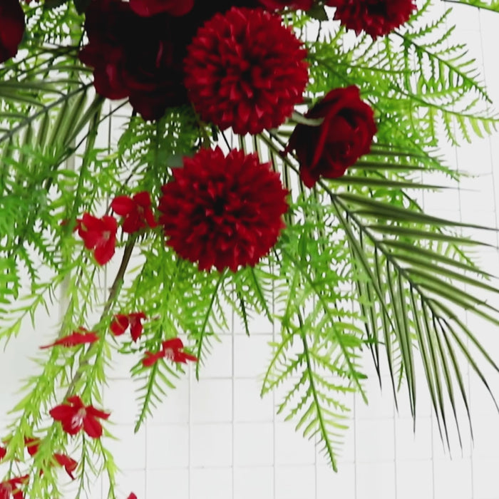 Burgundy floral swag with greenery and palm leaves for wedding decor.