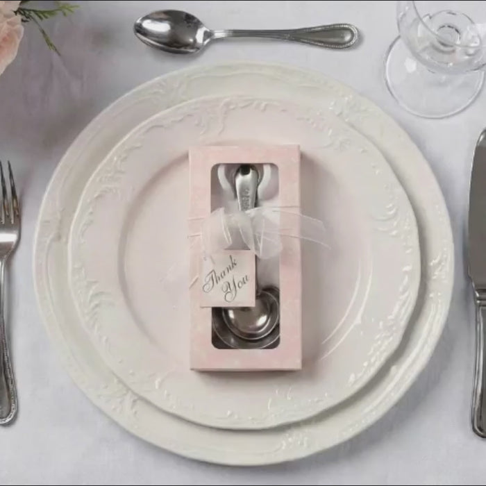 Engraved silver heart measuring spoons in a gift box on a decorative plate.