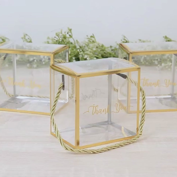 Clear cube gift boxes with gold trim and rope handle.