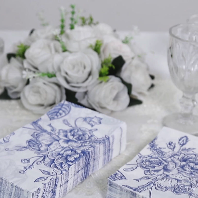 White napkins with blue French toile floral pattern on a table setting.
