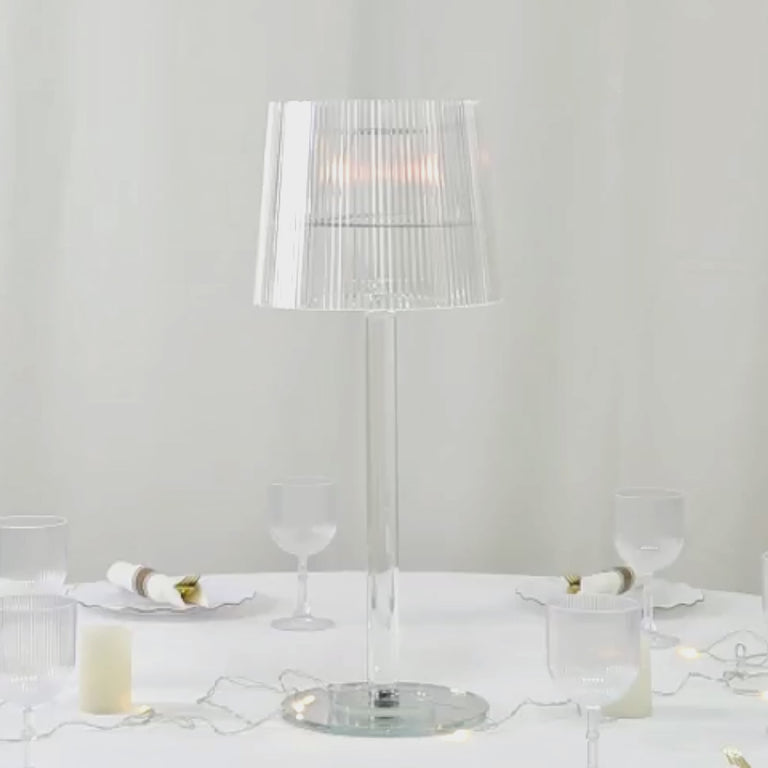 Clear acrylic candle lamp with ribbed shade on a table setting.