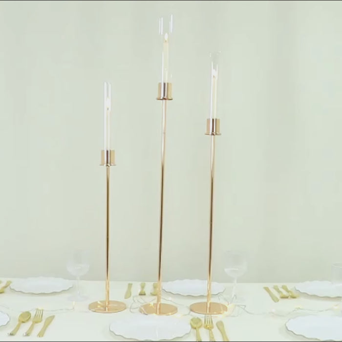 Gold metal taper candle holders with hurricane glass shades, modern minimalist design.
