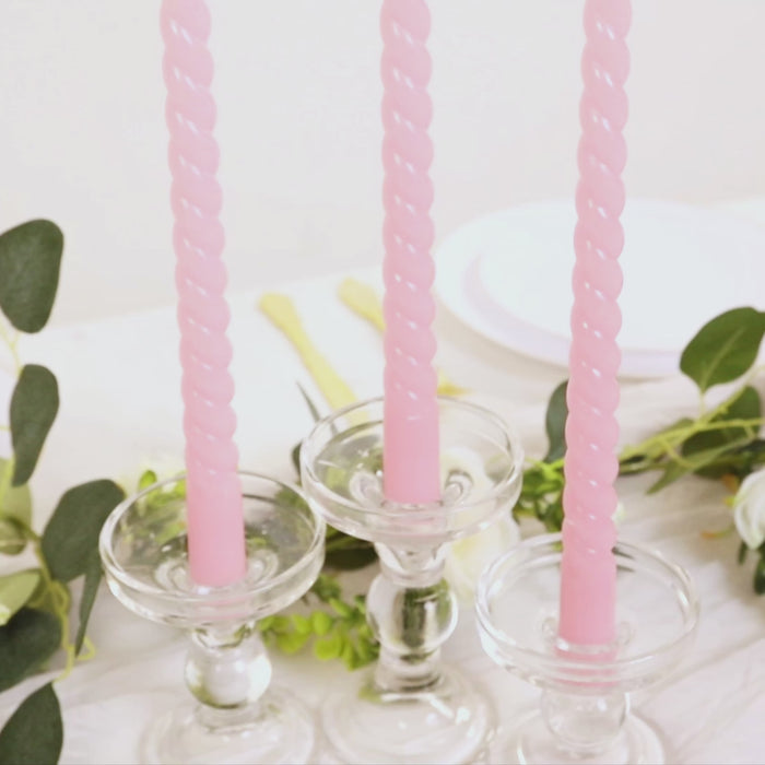 Pink taper candles in glass holders on a table with greenery.