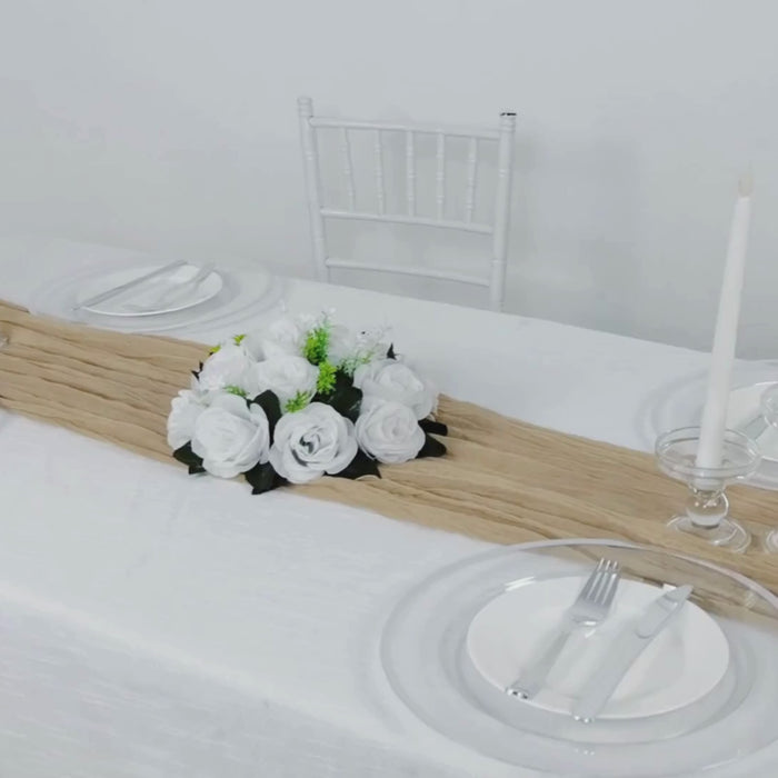 Beige gauze cheesecloth table runner on a white table with floral centerpiece.