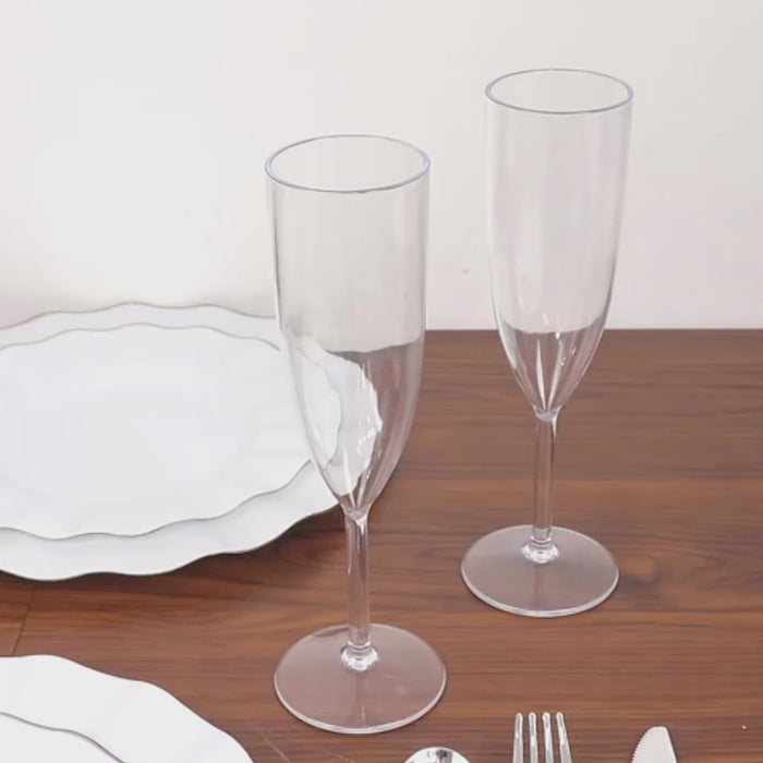 Clear shatterproof plastic champagne flutes on a wooden table.