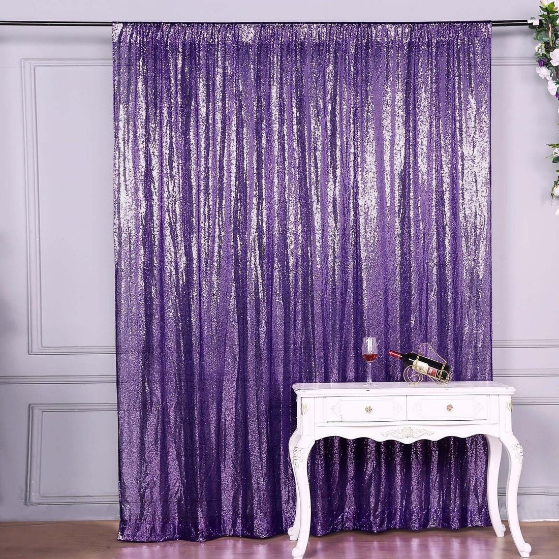 Purple sequin curtain draped in a staged setting with a table and wine glass.