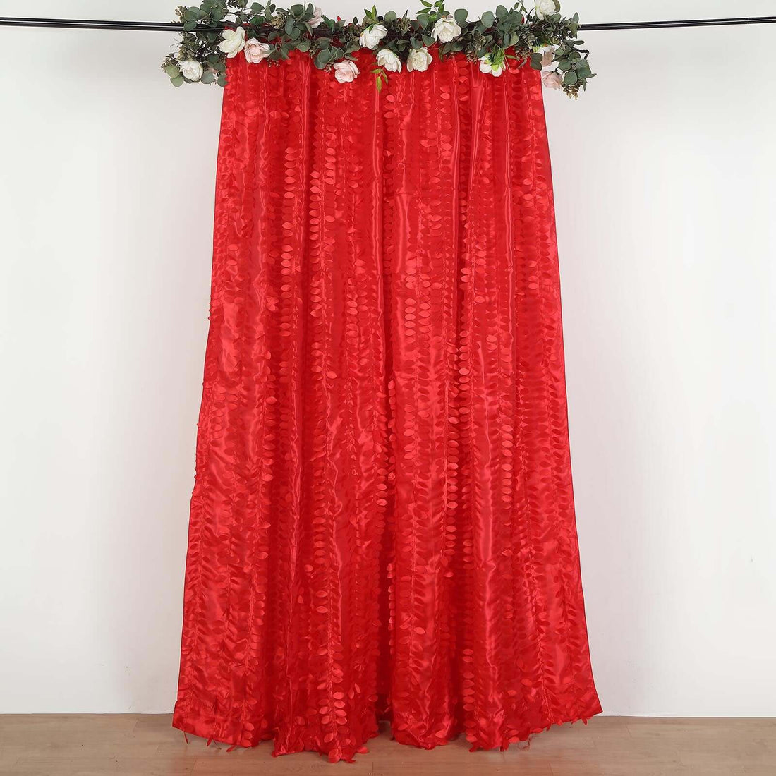 Red textured curtain with floral garland on top, hanging against a plain background.