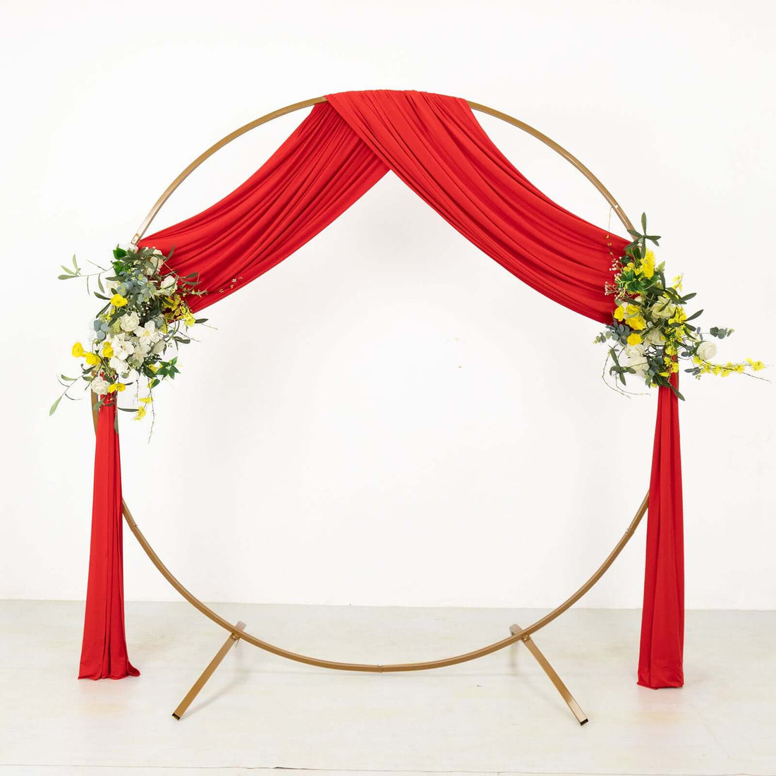 Red draped wedding arch with floral arrangements on a gold circular frame
