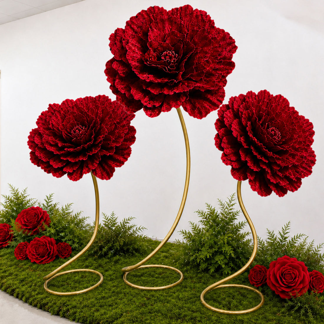 Red artificial flower topiary display with gold stands and green moss backdrop