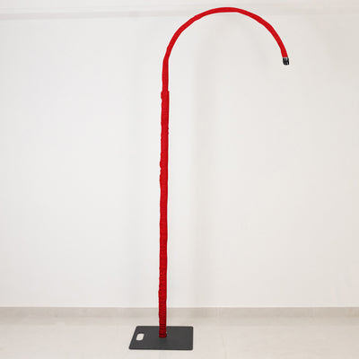 Red curved floor lamp with tall stand on a black base against white wall