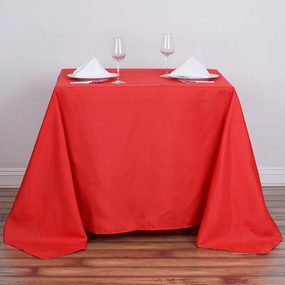 Red tablecloth set with glasses and napkins on a wooden floor.
