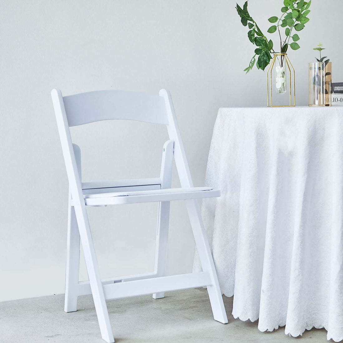 White folding chair next to a table with a plant and decorative items.