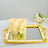Gold-framed mirror tray with candles and flowers on a wooden table.