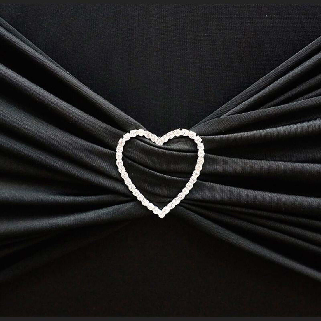 Heart-shaped rhinestone brooch on black fabric.
