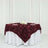 Burgundy rose-patterned tablecloth draped over a round table with white accents.