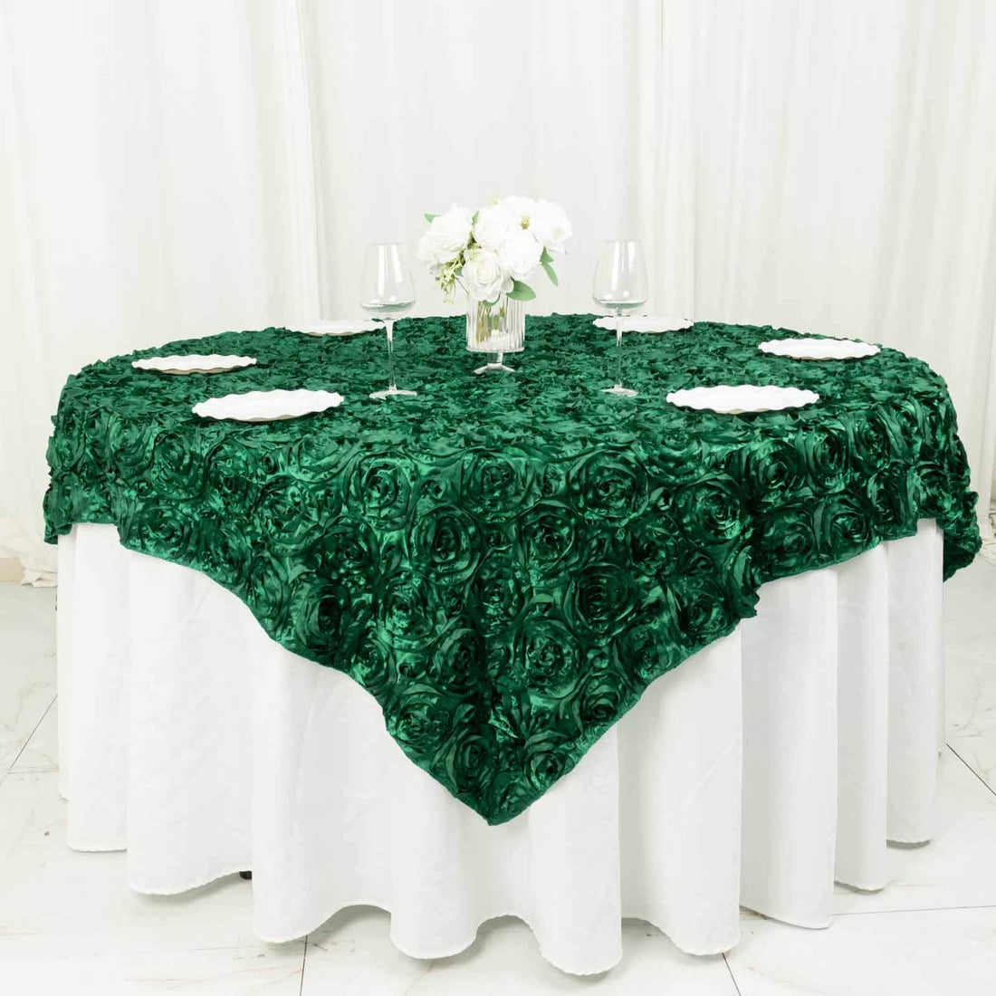 Green rose-patterned tablecloth draped over a round table with floral centerpiece.