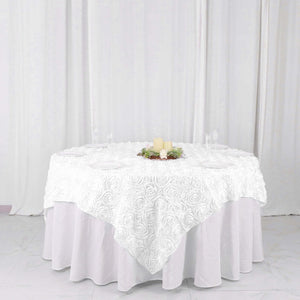 White rose-patterned tablecloth on a round table with candles and floral centerpiece