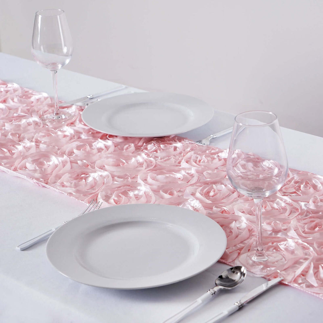 Elegant pink rose table runner with plates and glasses set for dining.