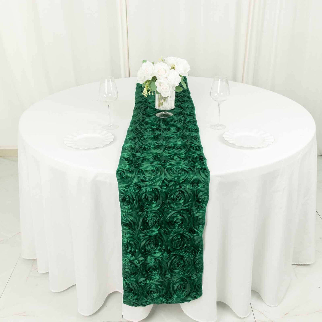Green rose-patterned table runner on a round white table with flowers and glasses.