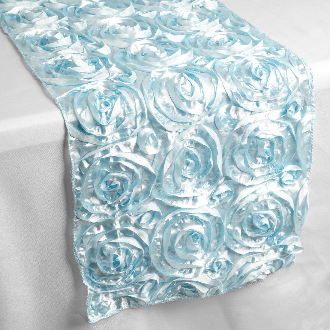 Light blue satin rose table runner on a plain surface.