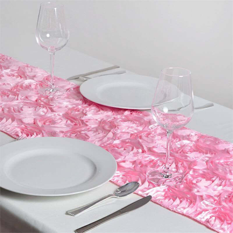 Pink satin table runner with elegant floral design, styled with plates and glasses.
