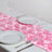 Pink satin table runner with elegant floral design, styled with plates and glasses.