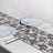 Silver rose table runner with two plates and wine glasses set for dining.