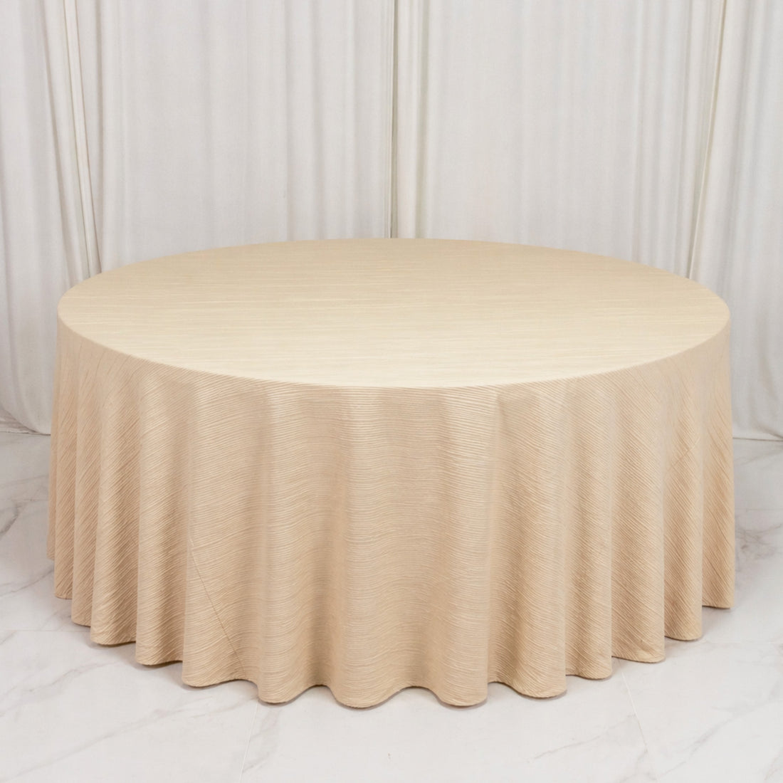 Round beige draped table with pleated skirt on white marble floor

