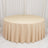 Round beige draped table with pleated skirt on white marble floor
