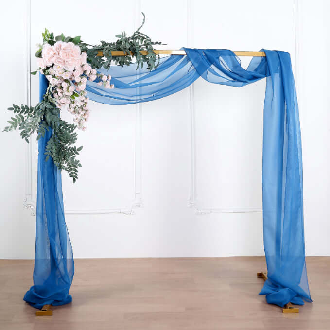 Blue draped wedding arch with floral accents on a plain background.