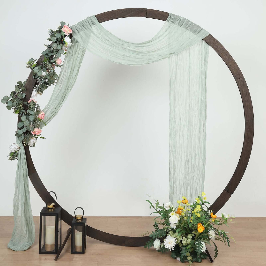 Decorative floral hoop with draped fabric and lanterns, styled for events.