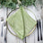 Green textured napkin elegantly folded on a decorative plate with silverware. #whtbkgd