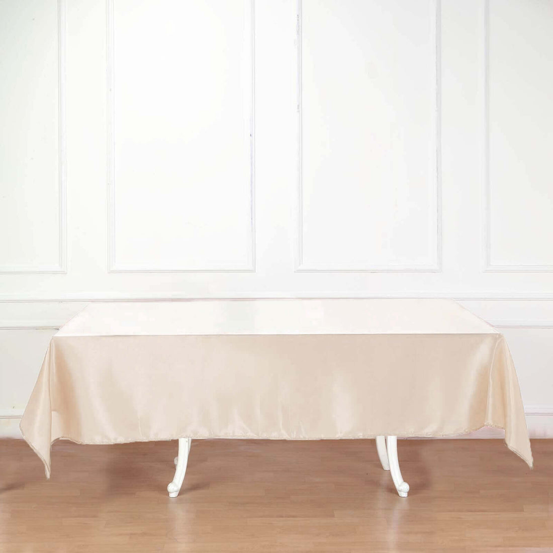 Beige satin tablecloth draped over a white table in a bright room.