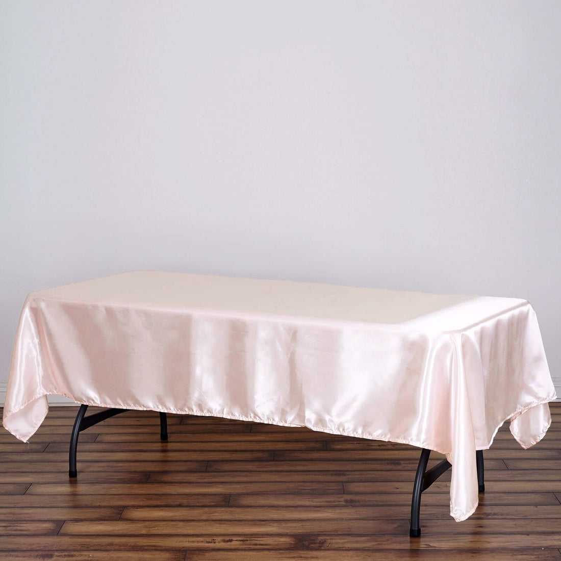 Pink satin tablecloth draped over a table on a plain backdrop